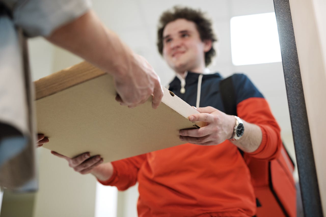 about-02 Smiling deliveryman handing over pizza box indoors, offering service.